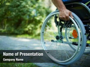 Close-up of male hand on wheel of wheelchair during walk in park PowerPoint Template